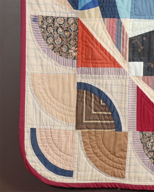 A cotton quilt made in geometric shapes which lends a very contemporary feel.  All of the fabrics are cotton, including the back which is in a navy tiny floral print with a rod pocket. The quilt has rounded corners, and is banded in a deep red