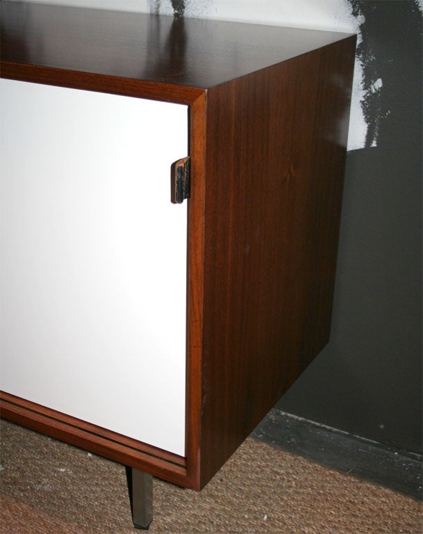 Classic walnut and white lacquer Florence Knoll sliding door credenza with leather pulls.  Cabinet has excellent interior storage, and rests on chrome legs.