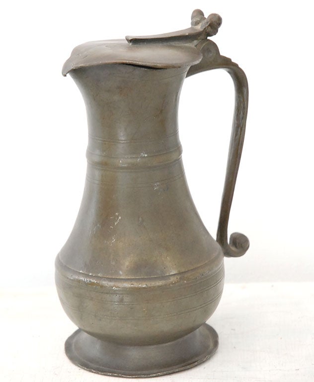 RARE ENGLISH PEWTER PITCHER W/ATTACHED LID.THE TOP OF LID HAS VARIOUS HALLMARKS .THIS PITCHER IS TEN INCHES HIGH W/ A WONDERFUL CURVED HANDLE.THE CODITION IS VERY GOOD AND HAS A NICE PATINA.