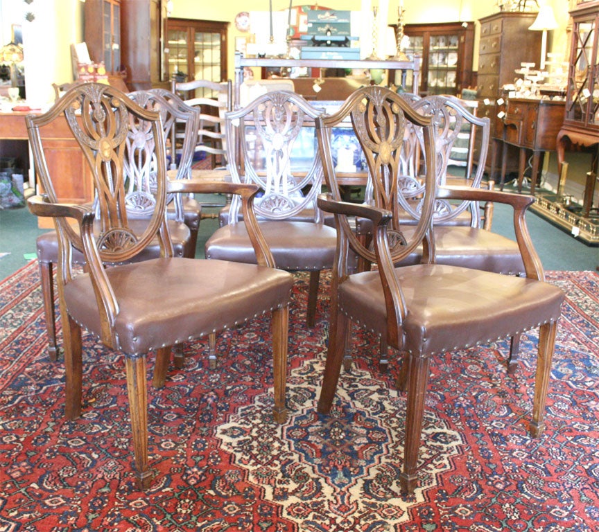 Eight mahogany chairs; two carvers and six sides; intricate carving on splats and shoulders; inlaid with boxwood and rosewood; later leather upholstery; in the Sheraton style with wheat and bell flower carving; tapered, carved legs ending in spade