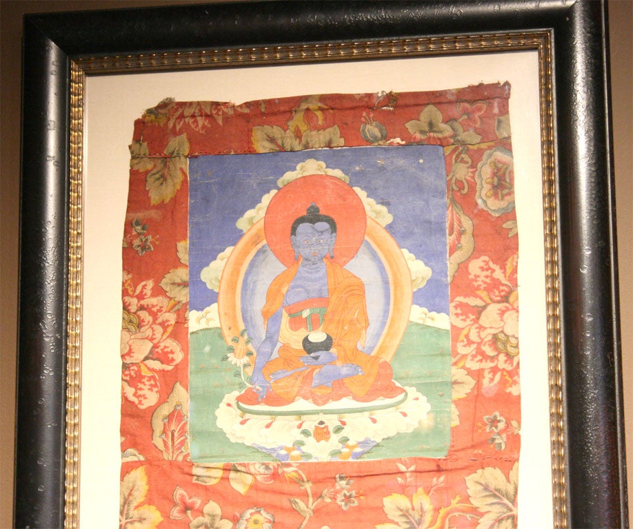 Framed hand-painted Tibetan Thangka with Medicine Buddha holding a blooming myrobalan plant in his right hand, and a begging bowl full of long life nectar in his left hand.  Painting is surrounded by a floral textile.<br />
<br />
Pagoda Red