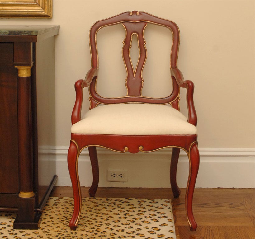 Comfortable arm chair painted red with gold trim, upholstered white linen