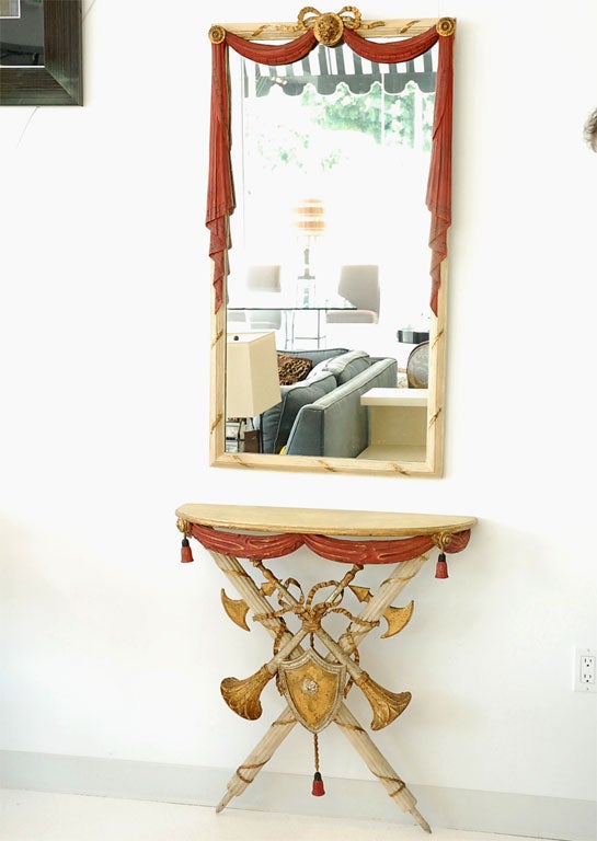 A decorative wall-mounted Italian console with matching mirror, featuring trompe l'oeil details- including swags and tassels, ropes and horns.  The console and mirror are carved wood and have been gessoed and polychromed.  The ribbon elements are