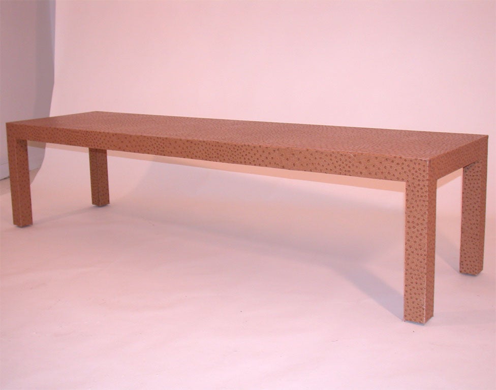 Traditionally proportioned coffee table after Karl Springer covered in a thick mid brown heavily textured and speckled faux ostrich skin upholstry.