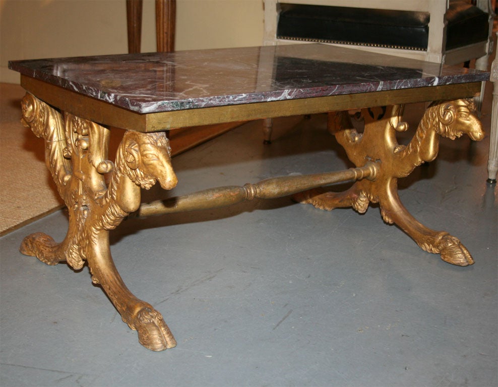 Low table comprised of rouge marble top resting on giltwood base with ram head supports ending in four hoofed feet.