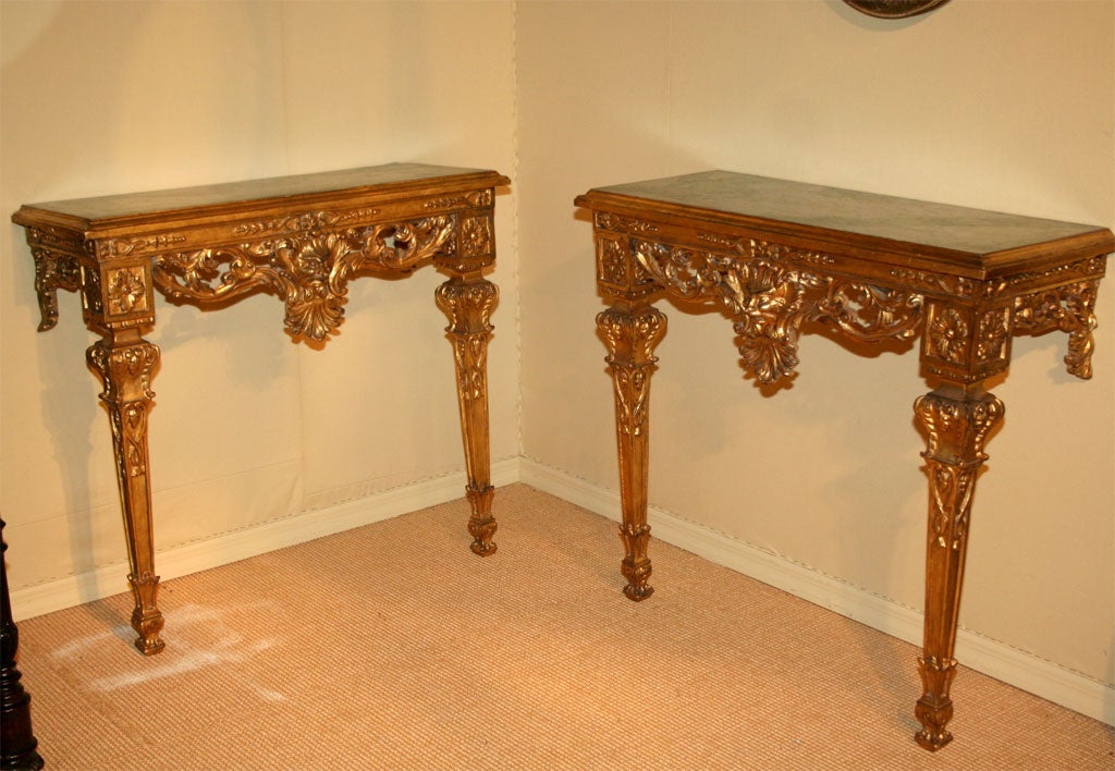 Pair of gilded Florentine consoles with painted faux marble recessed tops with foliate and grotesque frieze each raised on two four sided tapered legs.