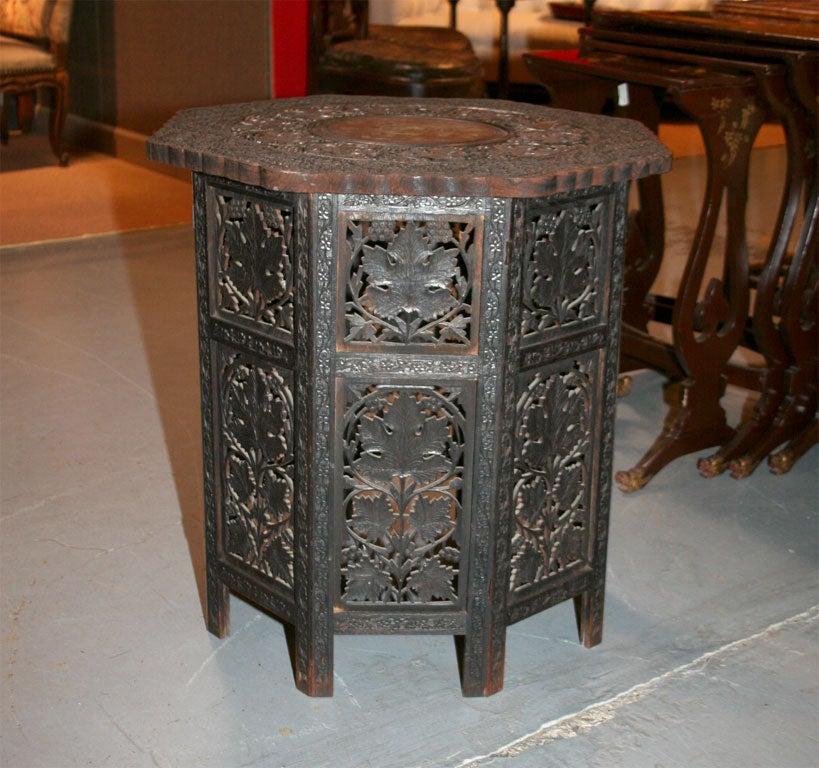 A carved octagonal table, the top consisting of tripartite design of floral, leaf and inlaid brass resting on pierced foliate folding base.  )