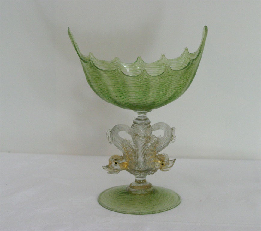 Hand blown oval centerpiece with optic rib and internally decorated green bowl and foot. The figural stem is further decorated with applied clear and gold leaf dolphins.