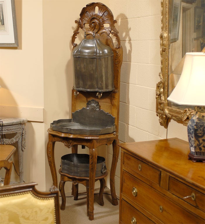 A Louis XV period Lavabo in walnut, with pewter basins and fixtures, dating from the mid-18th century. The piece is remarkable for retaining its original lower detached basin, pewter liners, and resevoir, all with only minor wear. The crisp carved