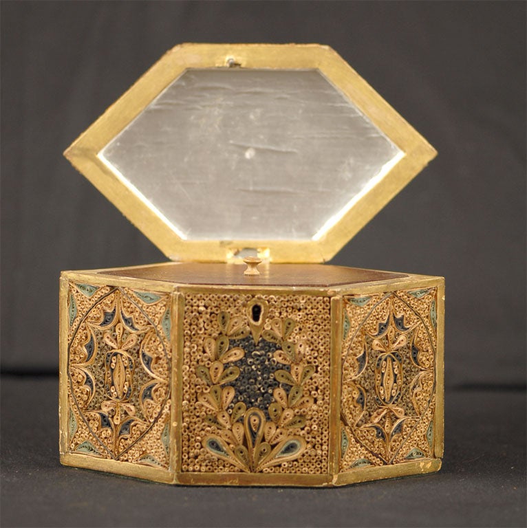 A Rolled-paper and gilt-wood Tea Caddy, in hexagonal form with beautiful designs on all sides formed in minute rolled strips of paper. The hinged top mounted with a metal handle, enclosing a foil-lined interior with a new inlaid wooden lid. <br