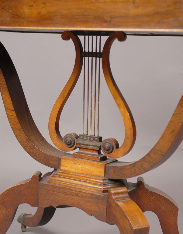 A beautiful Regency period game table in Rosewood with Satinwood inlay, and mounted on a Lyre-form pedestal base, ending in four splayed legs wih brass 'paw' formed castors. The table rotates to form a playing surface, with an interior concealed