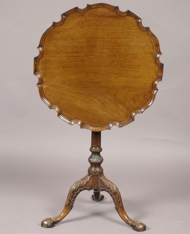A George III period pie-crust dessert table with a hinged top mounted on a bird-cage mechanism that allows for rotation. The table dating from the late 1700s, and supported by a carved pedestal and tripod base ending in ball-and-claw feet.  

