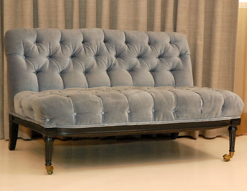 Pair of armless tufted settees in original blue velvet upholstery.  Decorative carved wood bases lacquered black with fine lided brass casters.
