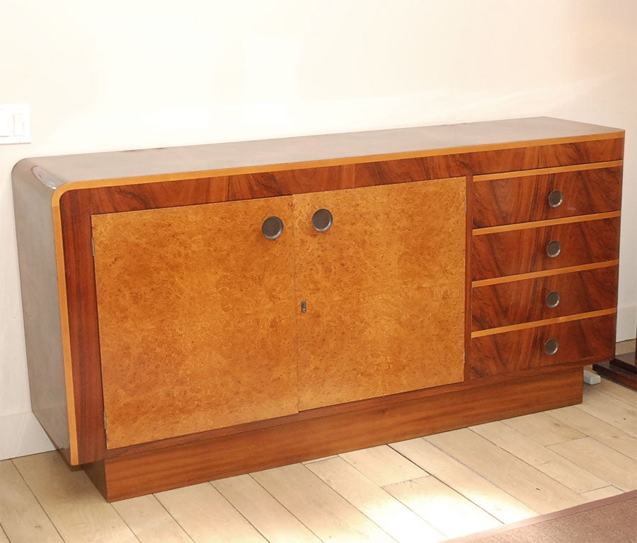 The rectangular rosewood cabinet or credenza with curved edges fronted with two large doors in bird's-eye maple, four drawers appointed with unusual dish-shaped metal hardware,  the whole raised on rectangular plinth base. Chic and modern vintage