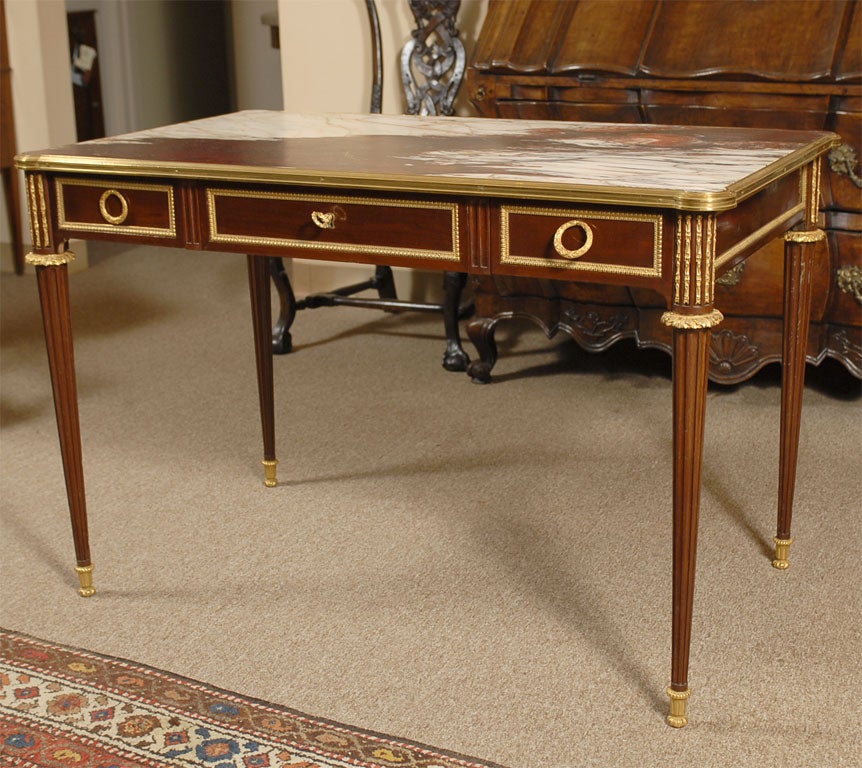 A fine Napoleon III period writing desk in mahogany, with gilt-bronze mounts and brass banding, the surface composed of an unusual and richly-colored marble top.

The deep red and white marble top resting within a brass border, above a mahogany