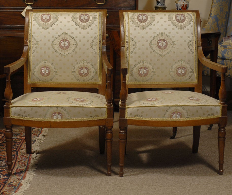 A pair of Directoire period walnut fauteuils/arm chairs with silk upholstery, turned tapered front legs and splayed back legs.