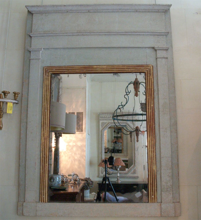 A Directoire mirror of the period, with a gray frame consisting of pilasters supporting the crown. The original mirror is set in an inner fluted and gilded frame.