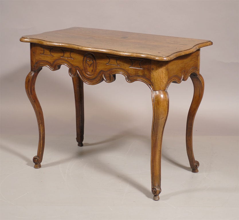 A Louis XV period console table in walnut, originating in Provence France. The walnut top mounted on a shaped apron, featuring molded designs that center on a carved heart. The body rests on four cabriole legs ending in scroll feet, each raised