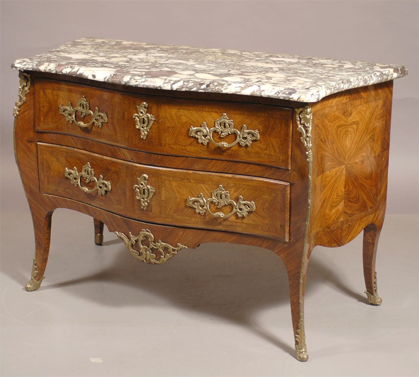 A Louis XV style French commode with a rich arranged kingwood and tulipwood exterior, mounted with gilt-bronze fixtures and Rococo accents, dating from the mid-1800s.

The bombe-form body with a conforming serpentine marble top, and composed of