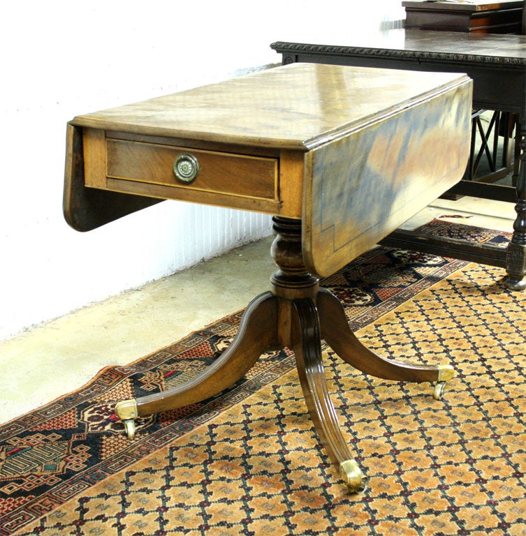 Polished mahogany dropleaf table with inlaid top and drawer front on turned pedestal over reeded, splayed legs ending in brass casters