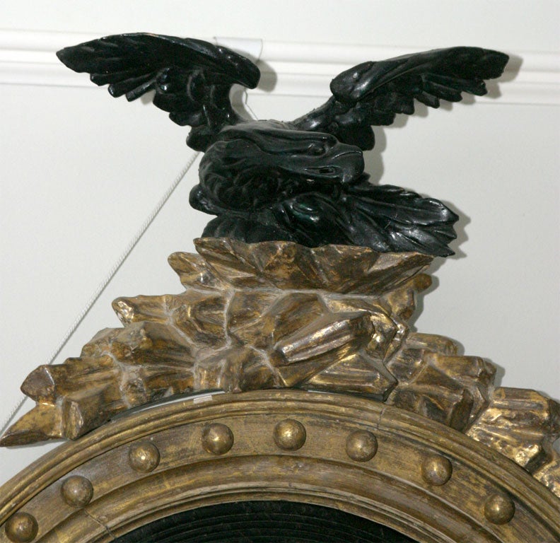 Regency giltwood convex mirror with ebonized reeded slip and cavetto set with balls; the top surmounted by an ebonized eagle with outstretched wings perched on a rocky ledge; carved shell, pineapple and foliage on lower crest.