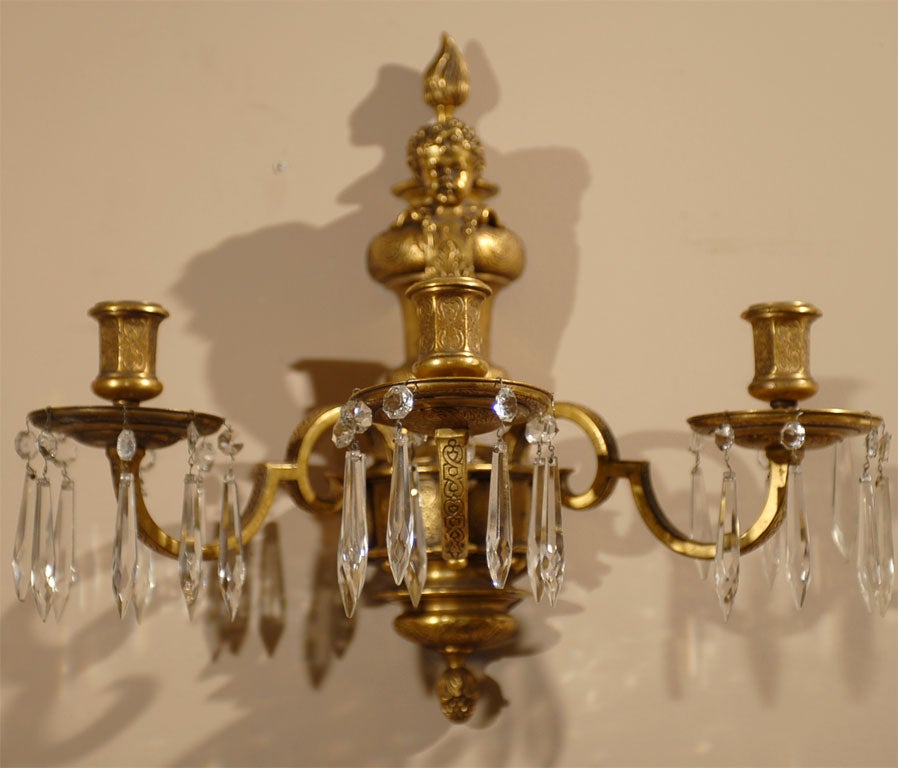 19th Century pair of heavily engraved French bronze wall sconces with the Flambeau urn shaped back plate surmounted with puttis having three scrolling arms fitted with crystal prisms.