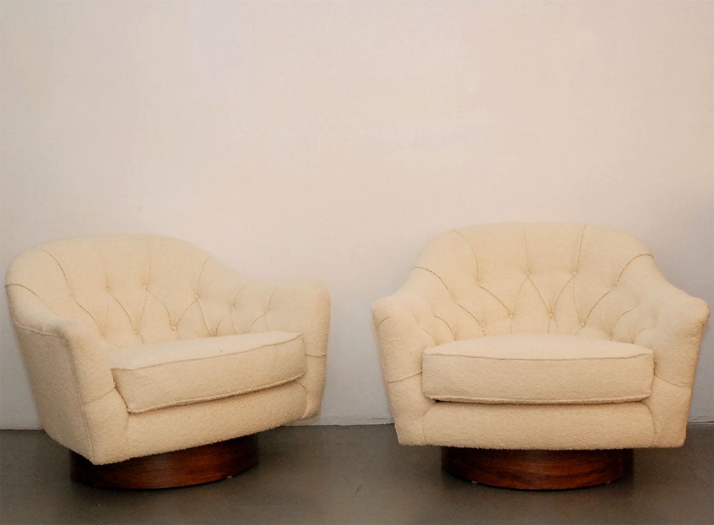 Pair of wide diamond tufted swivel chairs upholstered in creamy white wool boucle with walnut base.