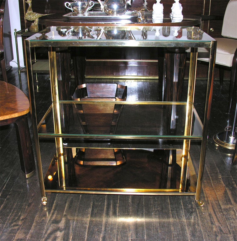 Bronze triple–tier bar cart with two clear glass shelves and one antique gold toned mirrored glass shelf on castors. By Jacques Quinet, French 1940s<br />
28” w, 16” d, 28 ½ “ h