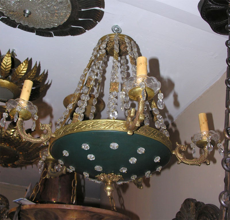 Lustre français de style empire, datant des années 1920, avec des inserts en cristal dans le corps et des chaînes en bronze et en cristal.

Mesures :
Hauteur : 20.5