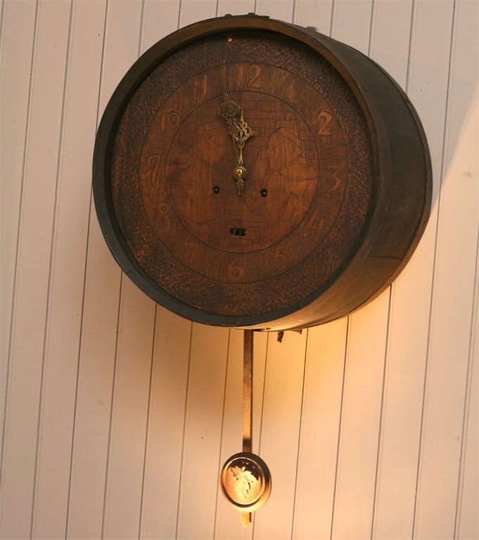 eight day wall clock in an oak barrel design with metal banding<br />
clock face incised with two monks drinking from steins<br />
brass hands - carved oak leaf pendulum<br />
key wind time & strike