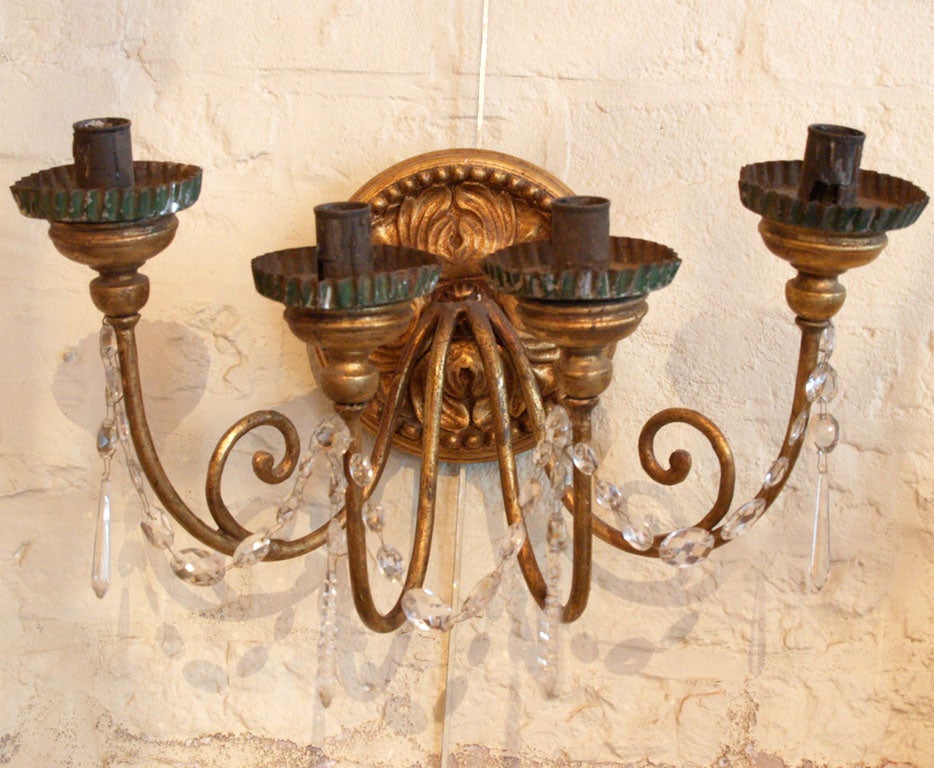 A pair of sconces with a bois dore circular medallion carved with acanthus leaves supporting 4 gilded iron arms. The arms are linked by crystal swags and topped with green painted bobeches. Wired for the US, they are fitted with beeswax sleeves.