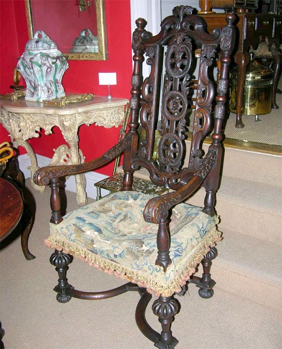 Carved walnut baroque armchair, the back with horsebone and foliate carving, over contemporary needlework seat, the fluted trumpet turned legs joined by 