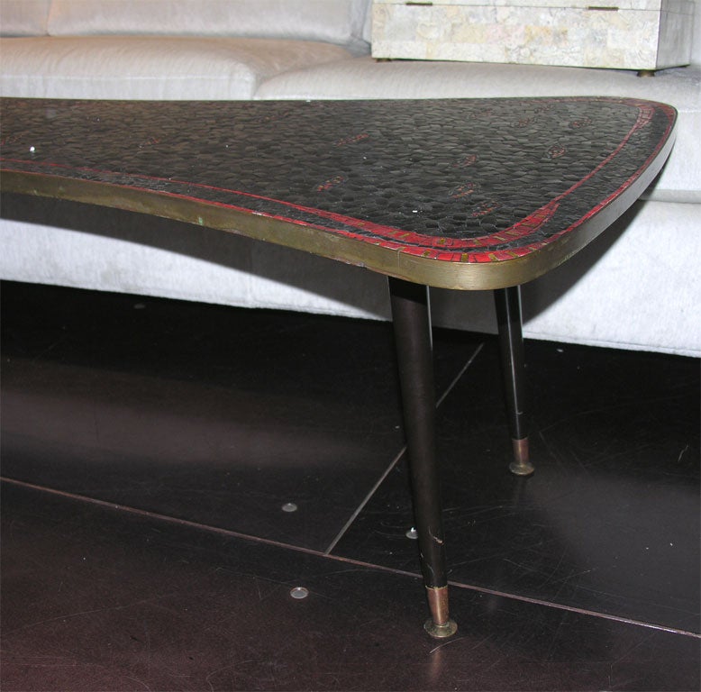 Red and black plastic mosaic cover the top of this unusual coffee table. A brass band is around the top edge of the table and four brass feet cap off the black legs.