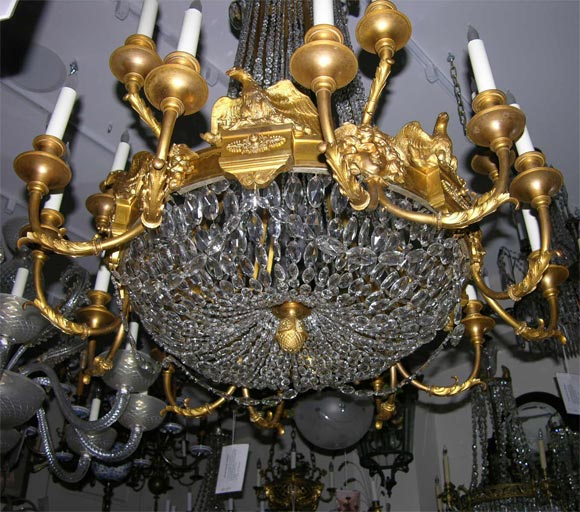 An 18 light French Empire style gilt bronze chandelier with cascades of graduated beads draped from upper ring with crystal drops and ring center with eagle mask motif.