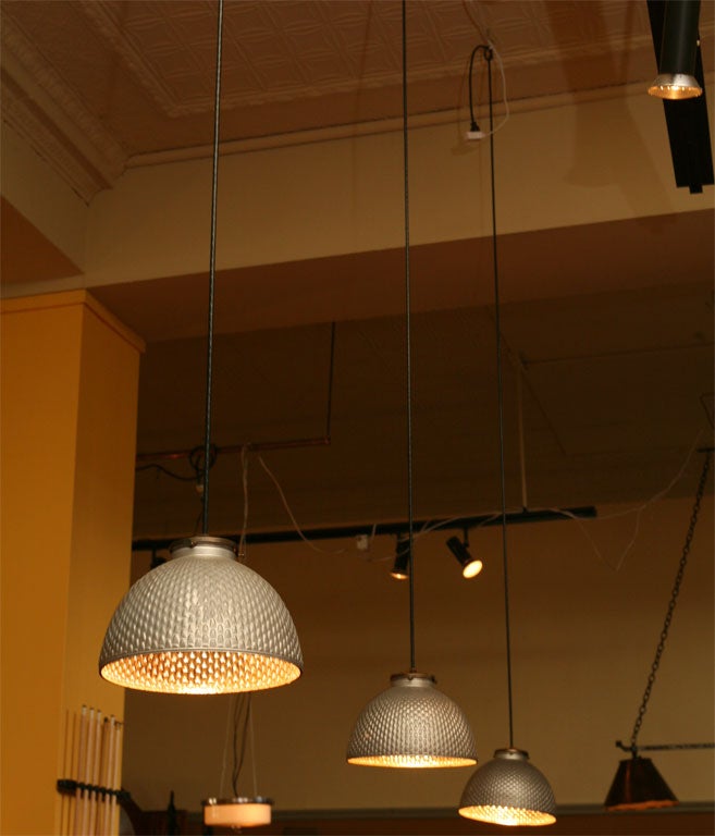 Hooded glass pedant fixture with mercury silver reflective interior, and matte silver exterior. made of pressed glass with a textured surface.New brass hardware and black rubber cording.3 available.