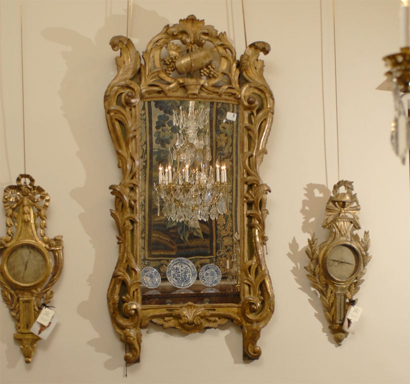 Impressively sized 18th century French Louis XV period mirror in giltwood mirror featuring elaborate carved Rococo designs and a rare wine trophy crest. Other than its impressive scale, the mirror's unique feature is the trophic crest consisting of