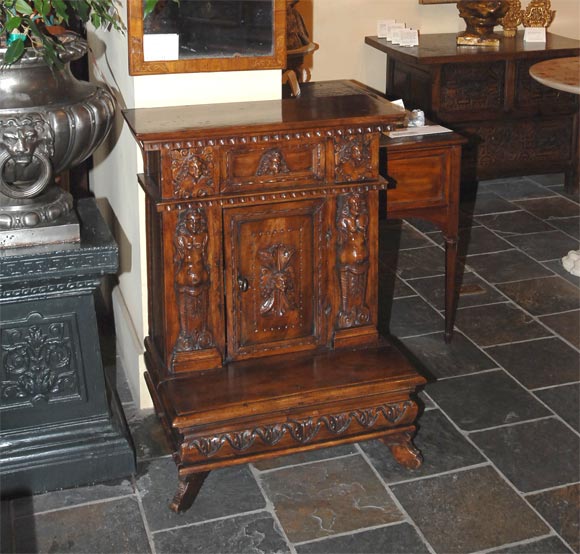 Italian Renaissance walnut prie-dieu, the rectangular top with a dentil-banded edge over a single drawer, flanked by ancient masks above a pair of terms, centering a bead-banded door, carved with a mask of a beauty over a hinged shelf with gadrooned