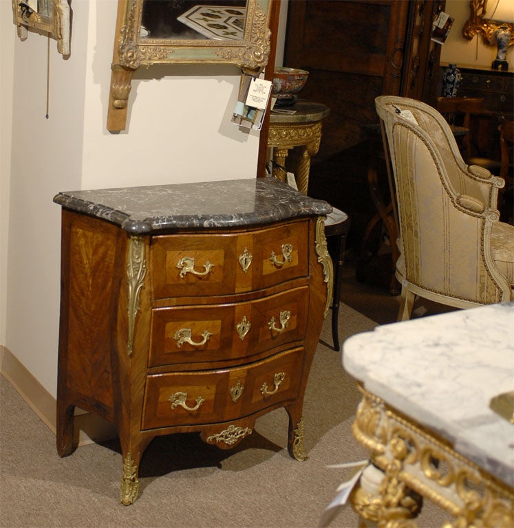 A petite Louis XV period serpentine commode in East Indian Rosewood & Kingwood, mounted with a mottled gray marble top, gilt-bronze mounts and hardware throughout, 3 drawers and  ending in saber feet. 

