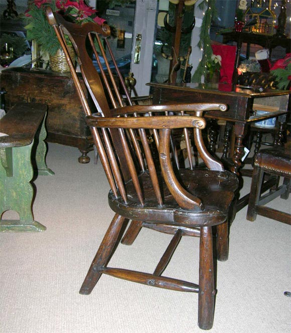 An English or Welsh oak windsor chair having marvellously carved ear backcrests and vase-shaped backsplat with thick elm hewn saddle seat on H-stretcher base.  A great example of a bold and characterful vernacular windsor arm chair.