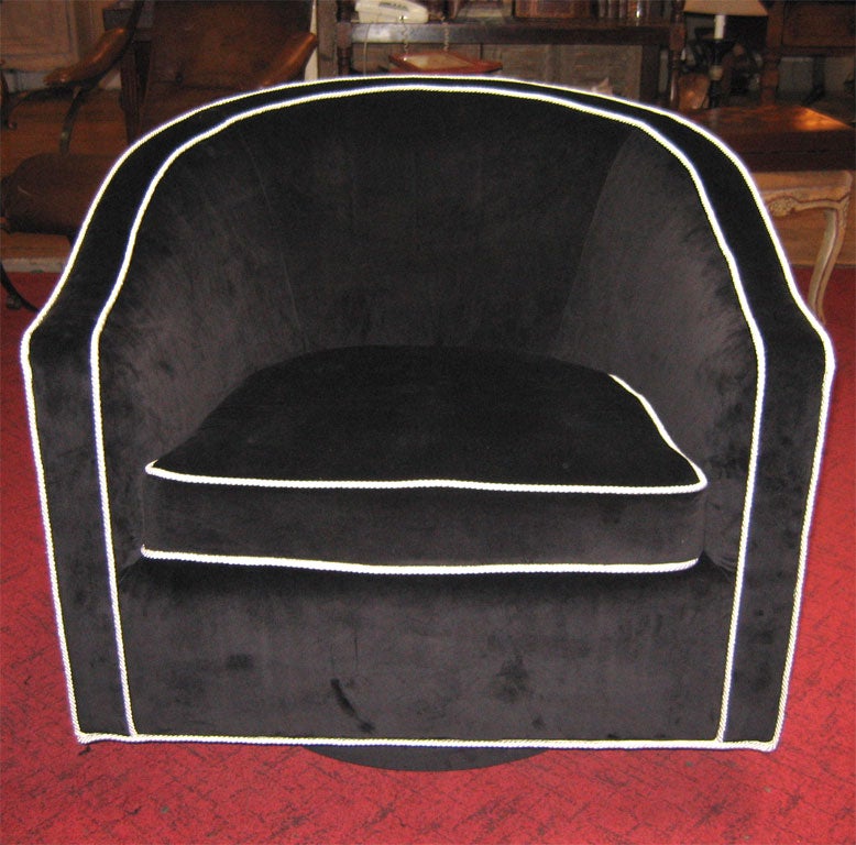 Two swiveling armchairs covered in black cotton velvet with white piping.