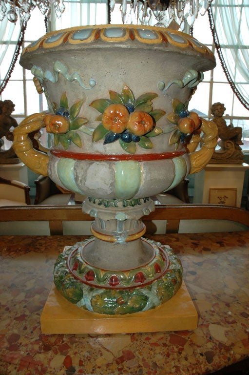 Sculpted two-handled urn with glazed painted ribbons, fruit and other neoclassical ornamentation. Two-pieces, marked 