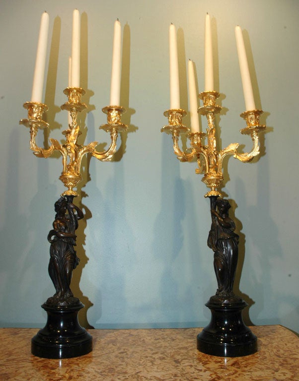 Pair of gilt-bronze and patinated bronze candelabra featuring neoclassical figures supporting four gilt-bronze arms.  Bases are black marble.