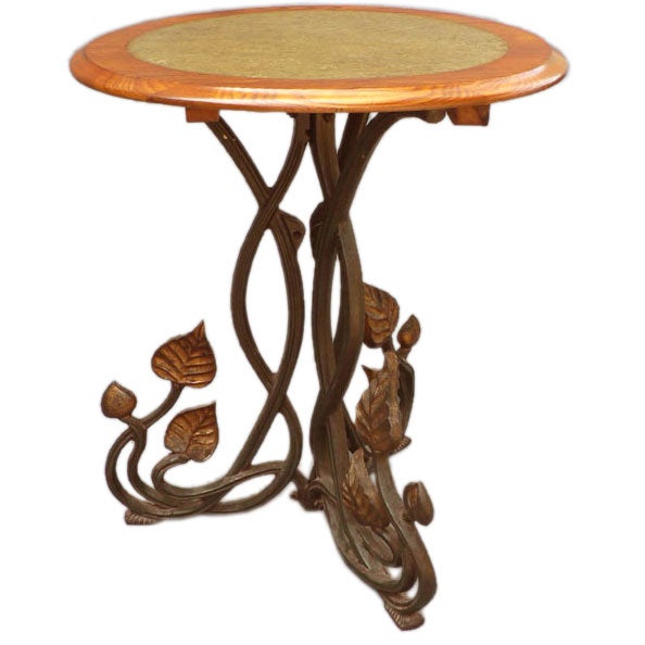 An Aesthetic period side table with a tripodal cast iron base in the form of vine-like elements and a circular oak top centered by a faux marble surface.