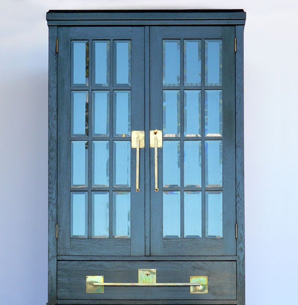 A German Jugendstil period cabinet executed in ebonized oak, with two-doors each with twelve pieces of inset beveled glass, above three drawers, all with extensive brass hardware. The beveled glass doors enclosing three interior shelves, circa 1915.