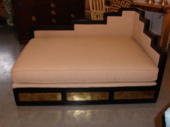 A laquered and upholstered asian style day bed withbras etched panels.