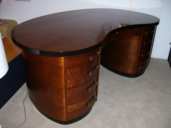A wonderful walnut kidney-bean-shaped American art deco desk from Gilbert Rohde. It has a great sculptural shape from front to back. Nine drawers.Two pull out table extensions.Bronze handles.Light hand polished.
