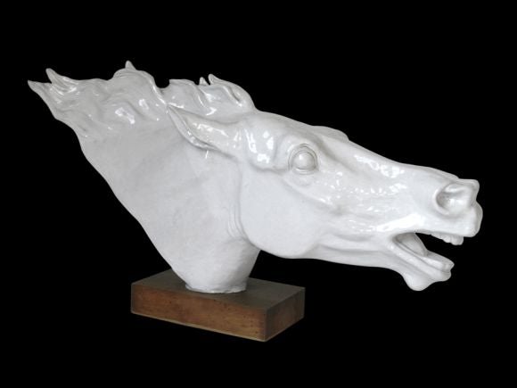 A DRAMATIC ITALIAN ART DECO IVORY-GLAZED POTTERY HORSE HEAD ON A WALNUT RECTANGULAR BASE. Of vibrant muscular form; the head and neck of the horse at a gallop; with widely flared nostrils over the open mouth of the large square jaw; wide