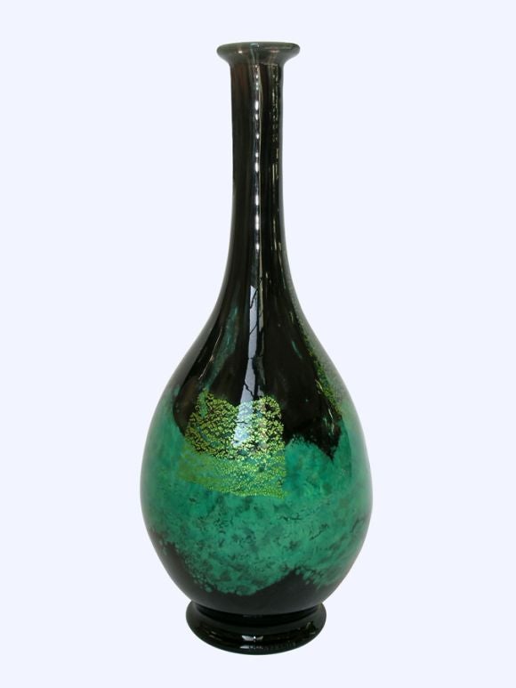 A ROBUST FRENCH BLACK AND GREEN GLASS LARGE BOTTLE-FORM VASE.Of globular form; with attenuated neck and everted lip; raised on a circular pad base; the whole of limpid black and jade blown glass with gold leaf highlights.<br />
For a tall vase of