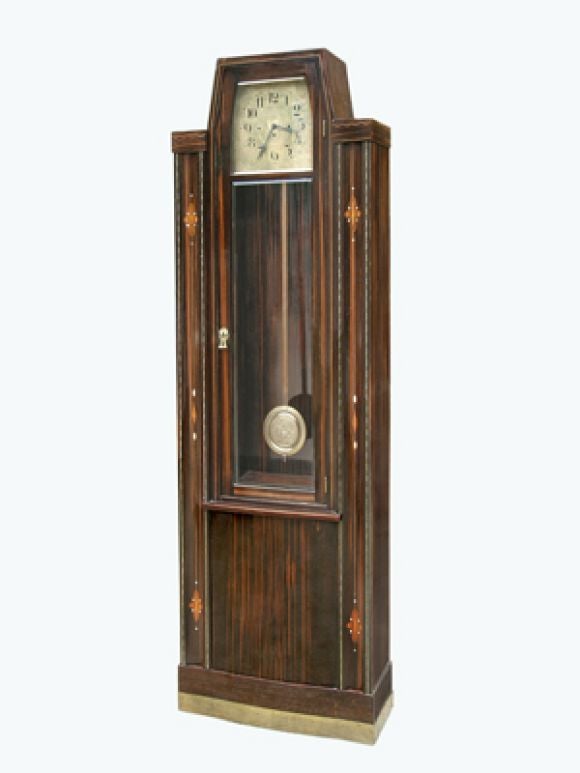 A MAGNIFICENT AUSTRIAN SECESSIONIST MACASSAR EBONY VENEERED AND INLAID TALL CASE CLOCK.The elongated U-form base with brass strip kick plate; the two tall rectiform sides centering and surmounted by the inset attenuated heptagonal case; the