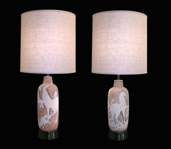 A SPIRITED COMPANION PAIR OF ITALIAN 1950’S HAND-WORKED CERAMIC LAMPS WITH HORSE AND HUMAN DESIGNS. Each vasiform lamp with erect neck upon a flaring circular brass base; the white ceramic etched with rearing horses over supine human figures evoking